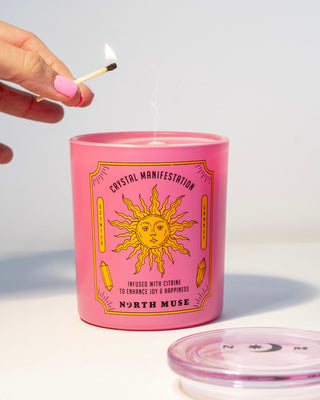 Hand lighting a North Muse 'Crystal Manifestation' candle in a pink jar with a sun design, infused with citrine.