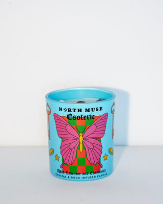 North Muse Esoteric candle in a blue jar with a pink butterfly design, infused with crystals, placed against a white background.