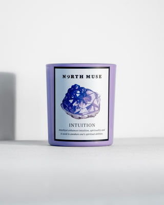 A North Muse "Intuition" candle in a light purple jar, featuring a blue crystal illustration on the label. The candle is set against a clean, minimalistic white background.