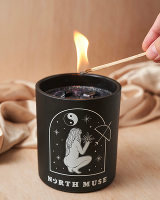 Hand lighting a North Muse black jar candle with celestial designs and dark, sparkly wax.