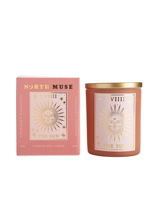 North Muse 'The Sun' candle with a celestial sunburst design in a pink jar, placed beside its matching box on a white background.