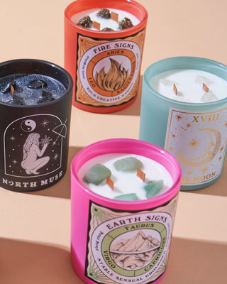 Four North Muse candles in various colors (black, orange, pink, blue) featuring different designs: celestial, Fire Signs, Earth Signs, and The Moon.