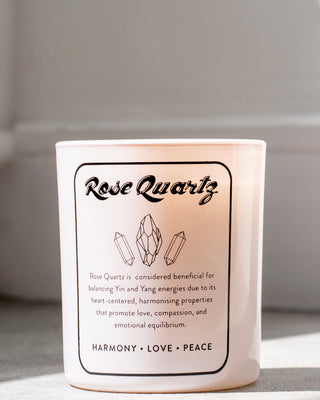 North Muse Rose Quartz candle with text describing the crystal's benefits for balancing Yin and Yang energies, promoting love, compassion, and emotional equilibrium. The candle label features illustrations of rose quartz crystals and the words 'Harmony, Love, Peace' at the bottom.